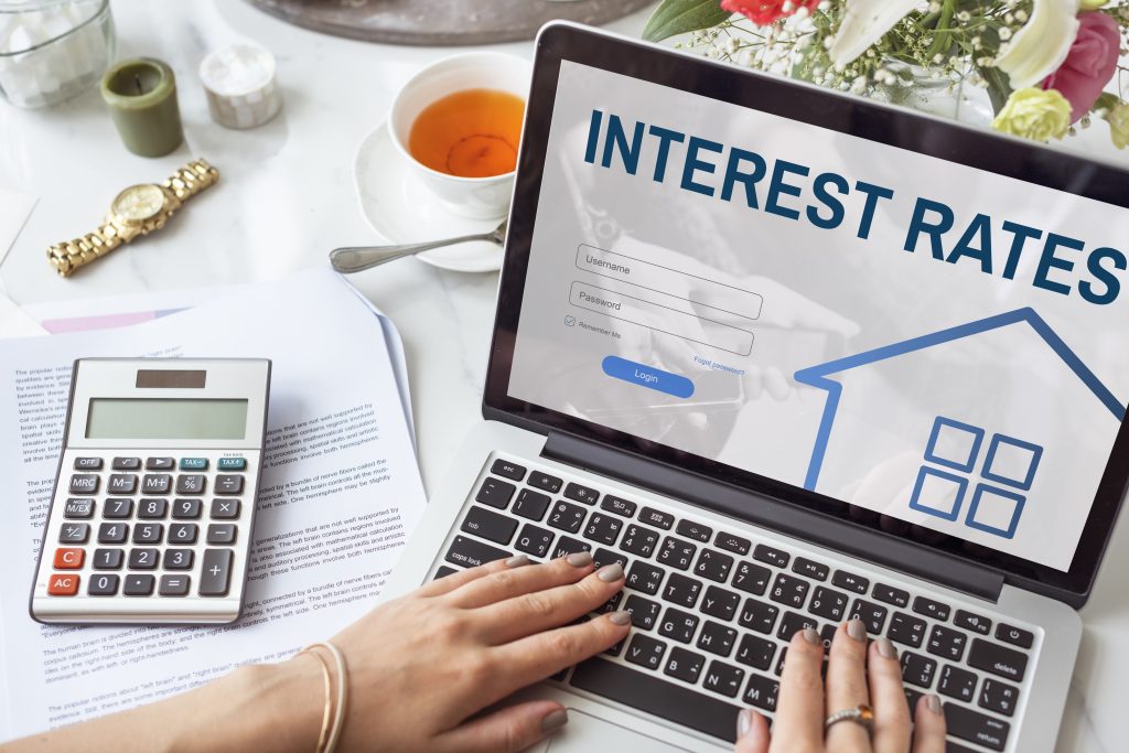 Checking current owner financing interest rates on a laptop, surrounded by home loan papers and a calculator.