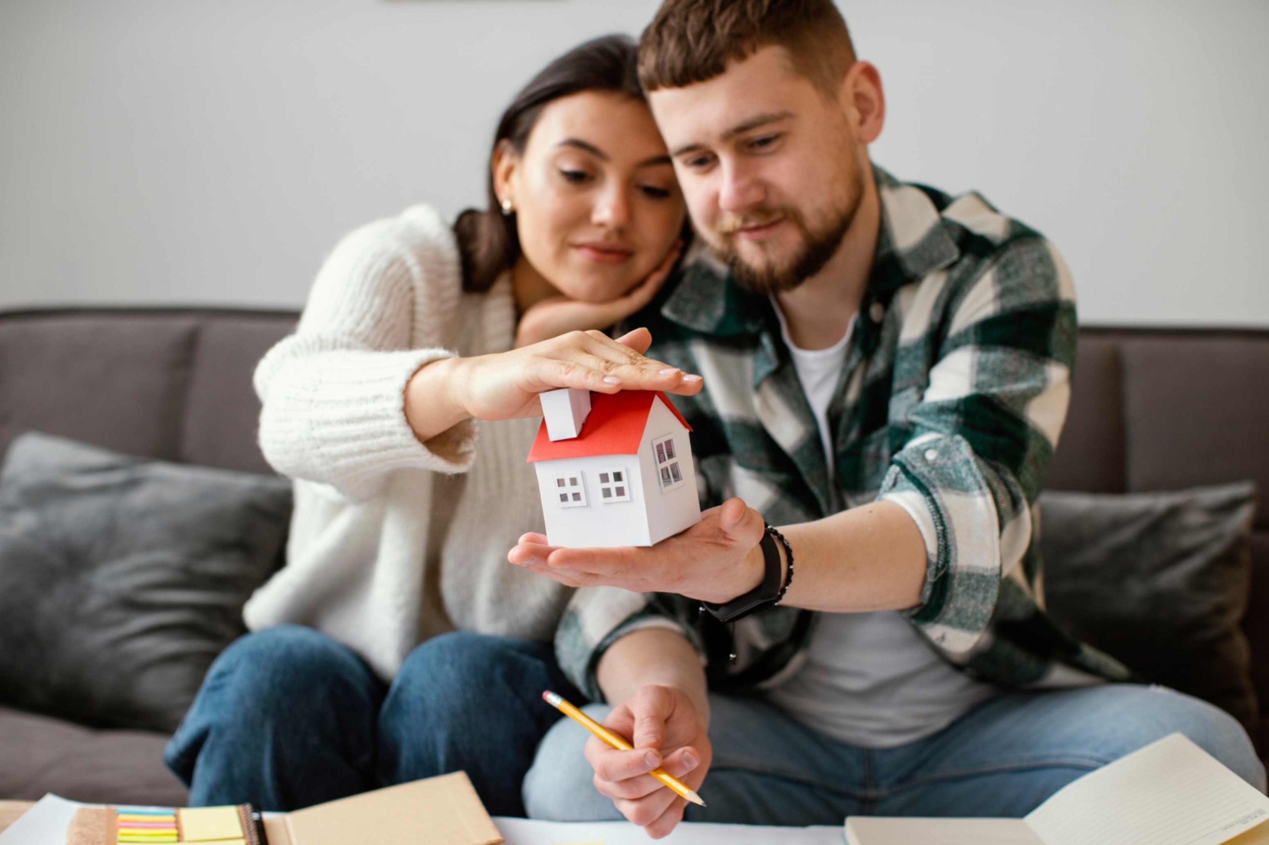 Young couple holding a miniature house model, symbolizing their start in multi-family real estate investing for beginners.