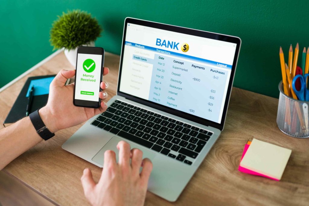 Person transferring funds using smartphone and laptop for online banking transaction