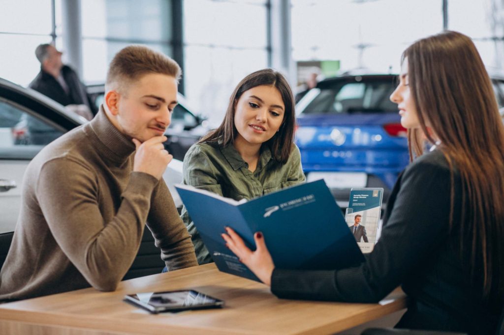 Young couple discussing financing options with a car dealership representative to understand the credit score needed to lease a car.