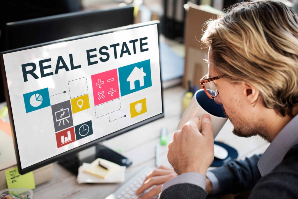 Man researching how to start a real estate investment business on a computer screen, analyzing finance and property icons while drinking coffee.