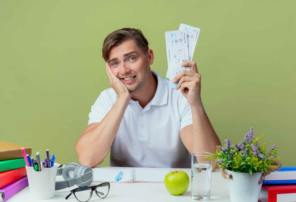 Happy young man holding travel tickets at a desk, representing the benefits of spending less money than budgeted